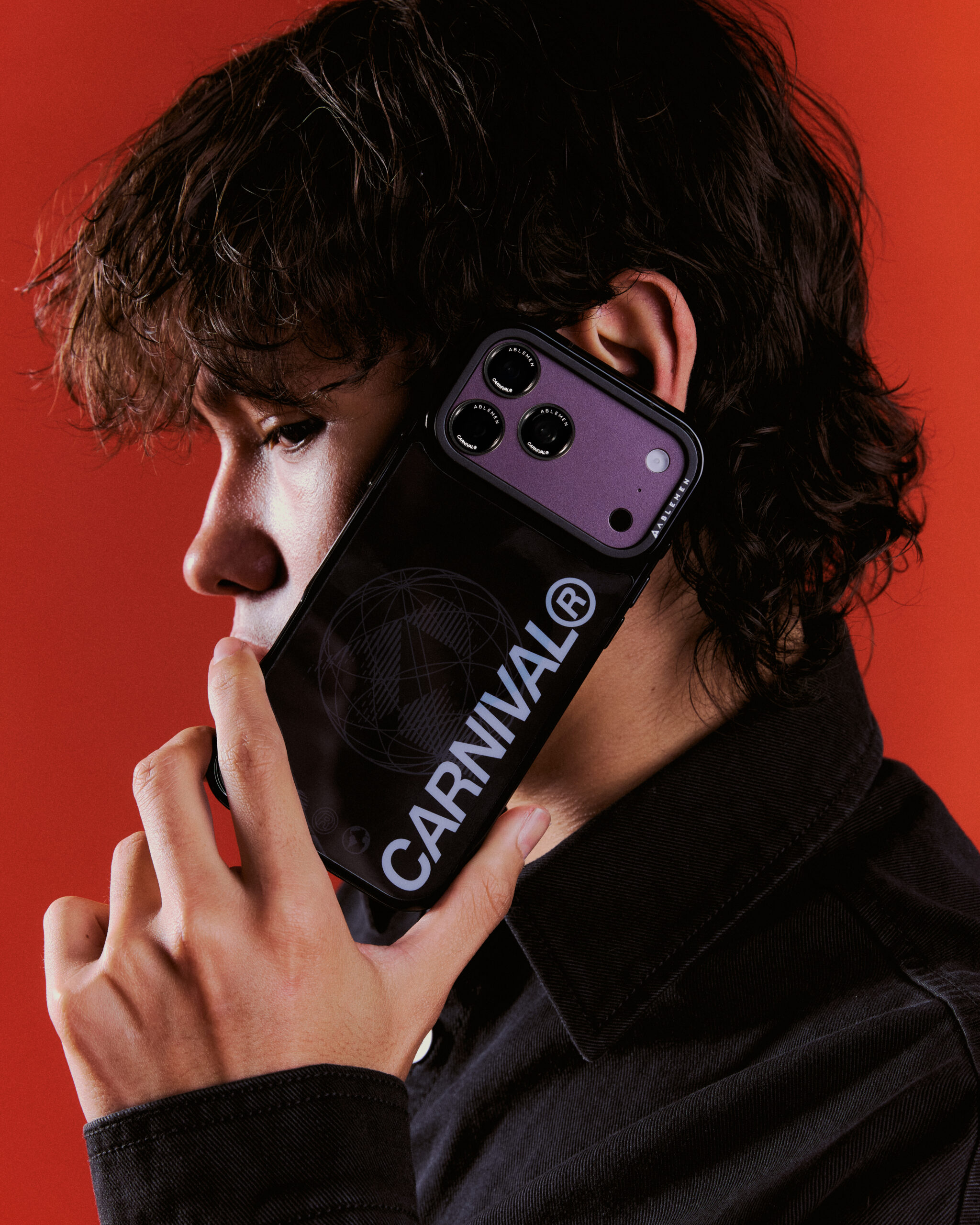 นายแบบถือโทรศัพท์พร้อมเคส CARNIVAL สีดำแนบใบหน้า บนฉากสีแดง