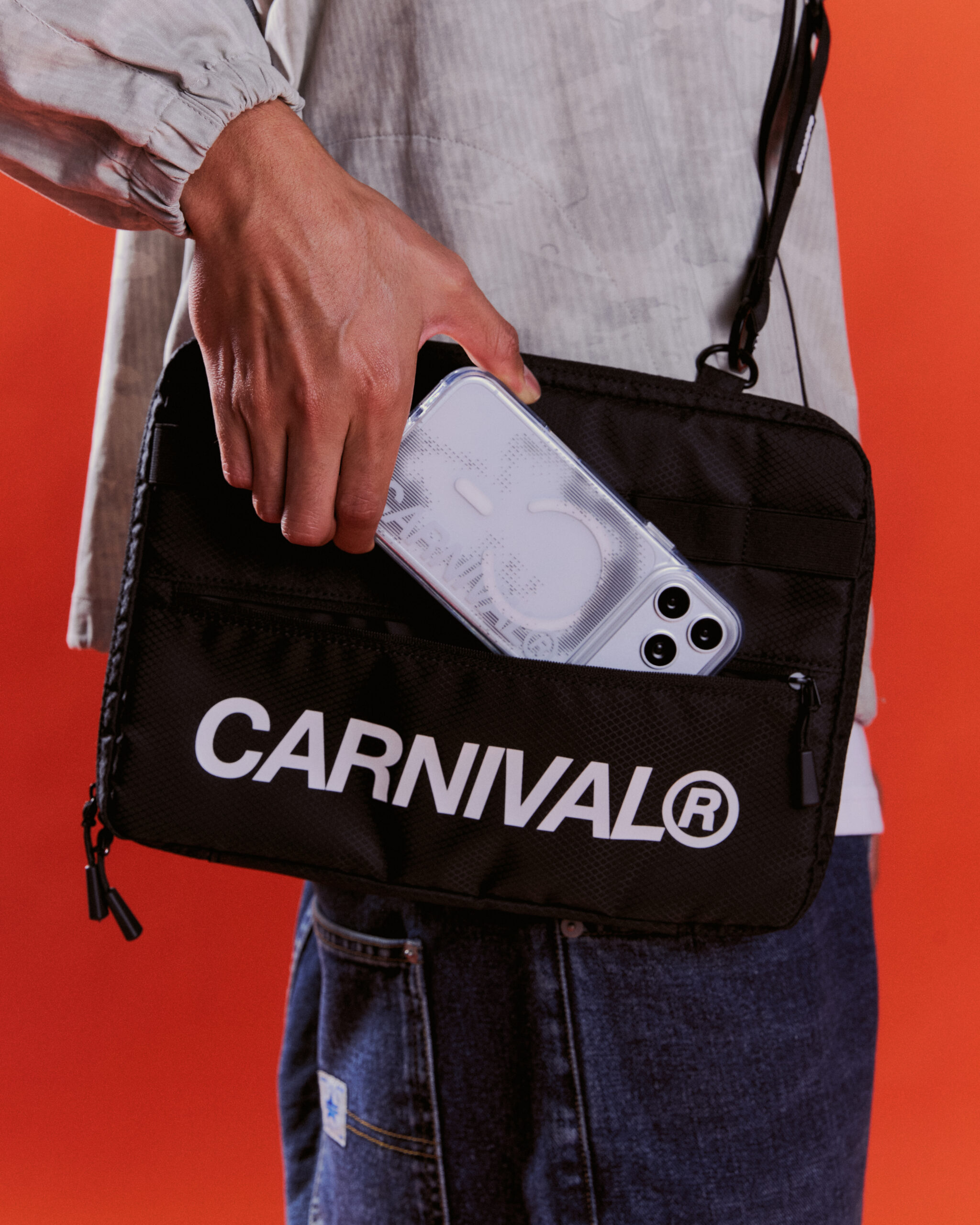 เคส CARNIVAL สีขาวในมือนายแบบ คู่กับกระเป๋าสะพายสีดำ
